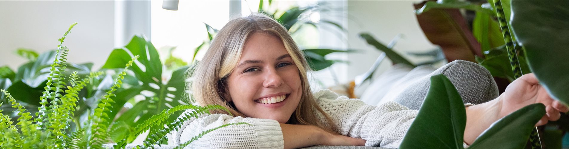Jungle Ambiente - Frau liegt auf Sofa zwischen Grünpflanzen Jungle Ambiente - Frau liegt auf Sofa zwischen Grünpflanzen